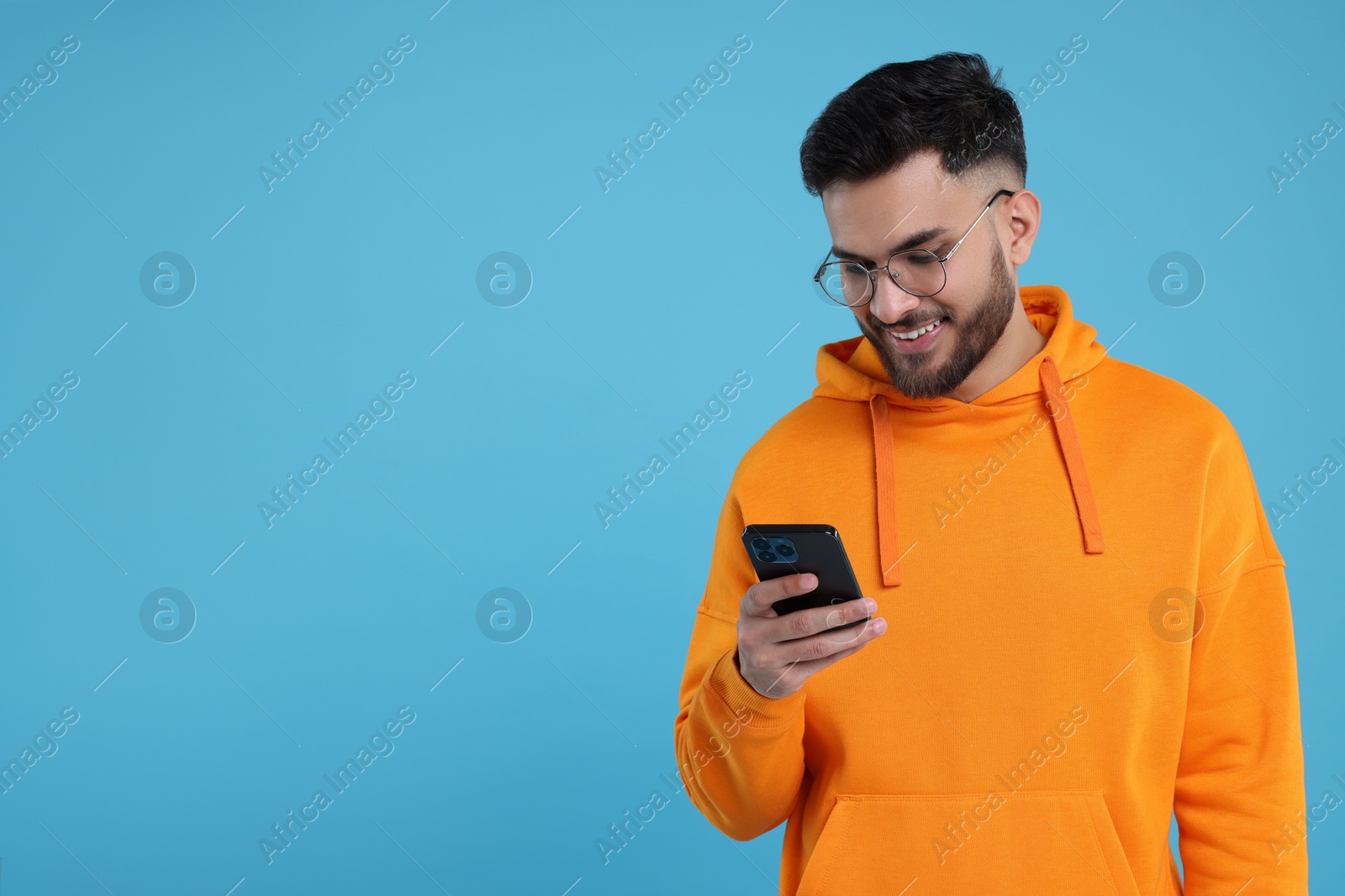 Photo of Happy young man using smartphone on light blue background, space for text