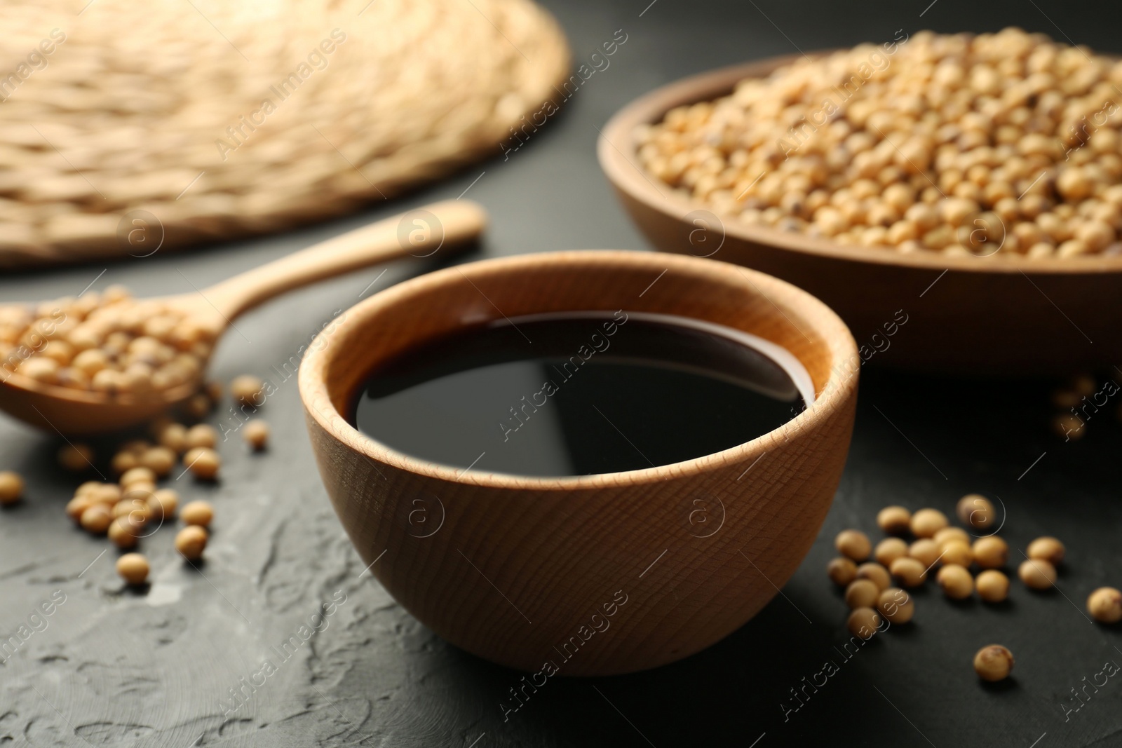 Photo of Tasty soy sauce in bowl and soybeans on black table, closeup