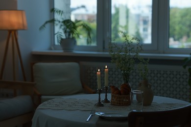 Photo of Clean dishware, flowers, fresh pastries and burning candles on table in stylish dining room