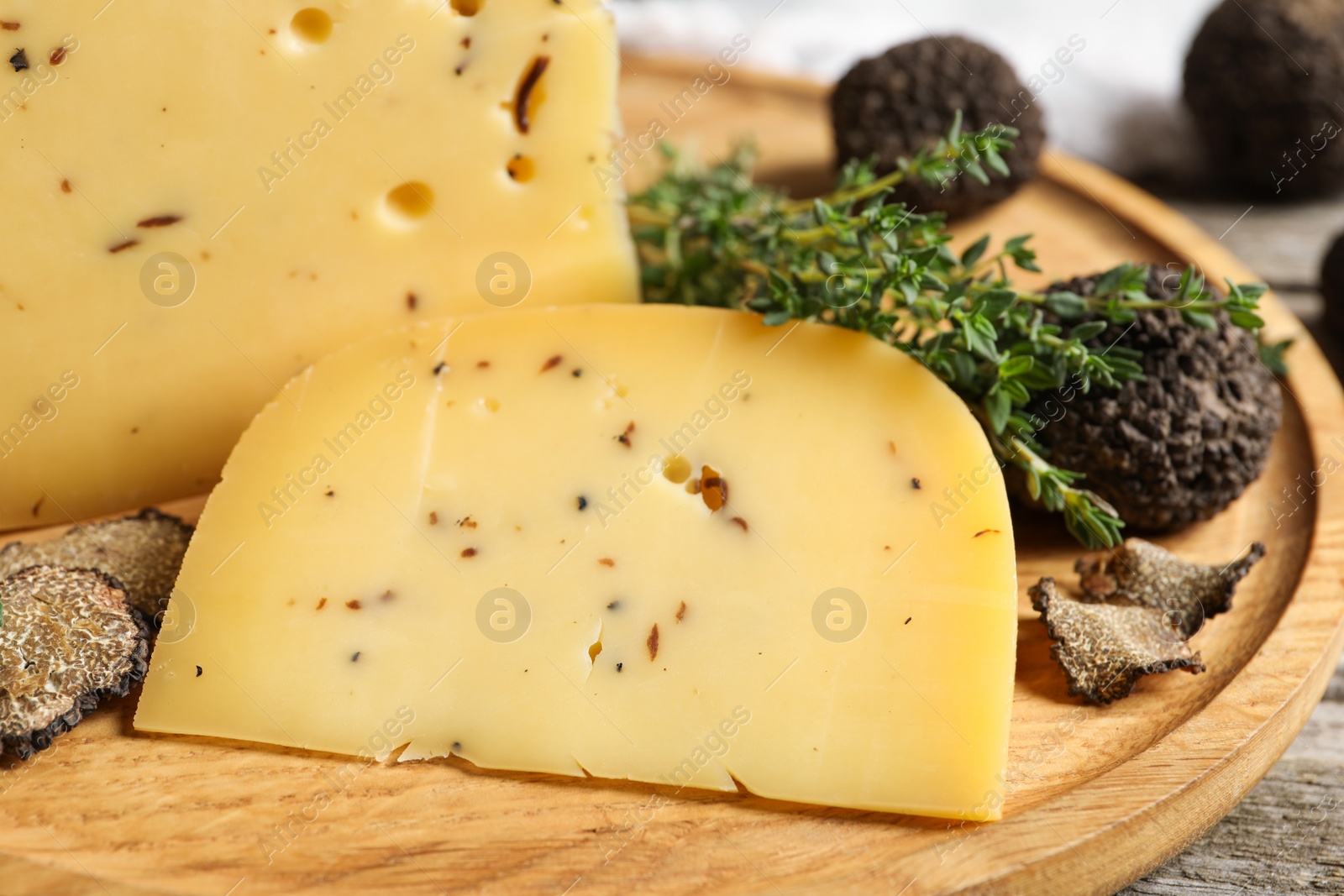 Photo of Delicious cheese, fresh black truffles and thyme on wooden plate, closeup