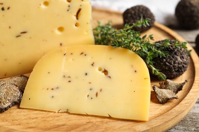 Photo of Delicious cheese, fresh black truffles and thyme on wooden plate, closeup