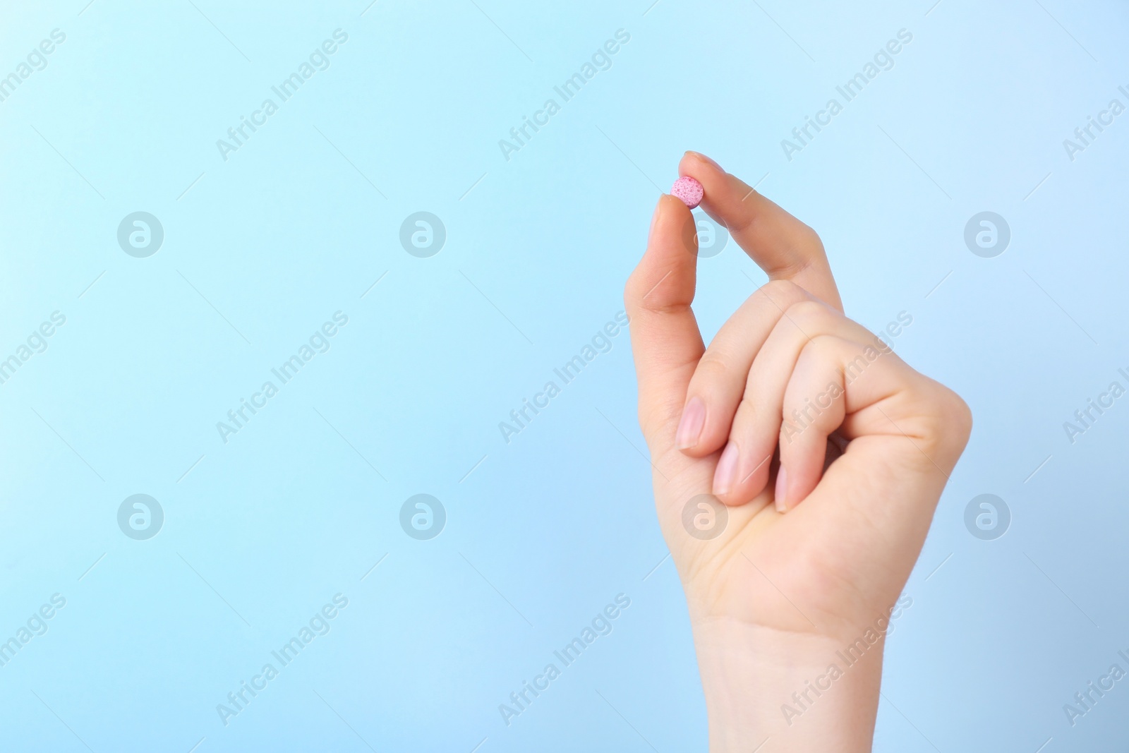 Photo of Woman holding vitamin pill on light blue background, closeup. Space for text