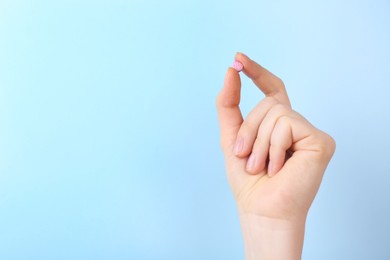 Photo of Woman holding vitamin pill on light blue background, closeup. Space for text