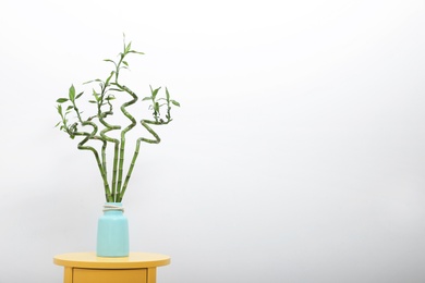 Photo of Vase with bamboo stems on yellow table against light wall, space for text