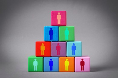 Team and management concept. Pyramid of colorful cubes with human icons on grey background