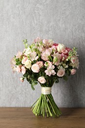 Photo of Beautiful bouquet of fresh flowers on wooden table near grey wall