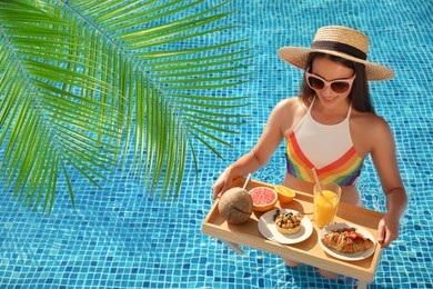 View of beautiful green tropical leaves and young woman with delicious breakfast on tray in swimming pool