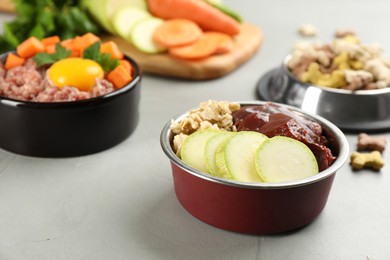 Natural pet food in feeding bowls on grey table, closeup