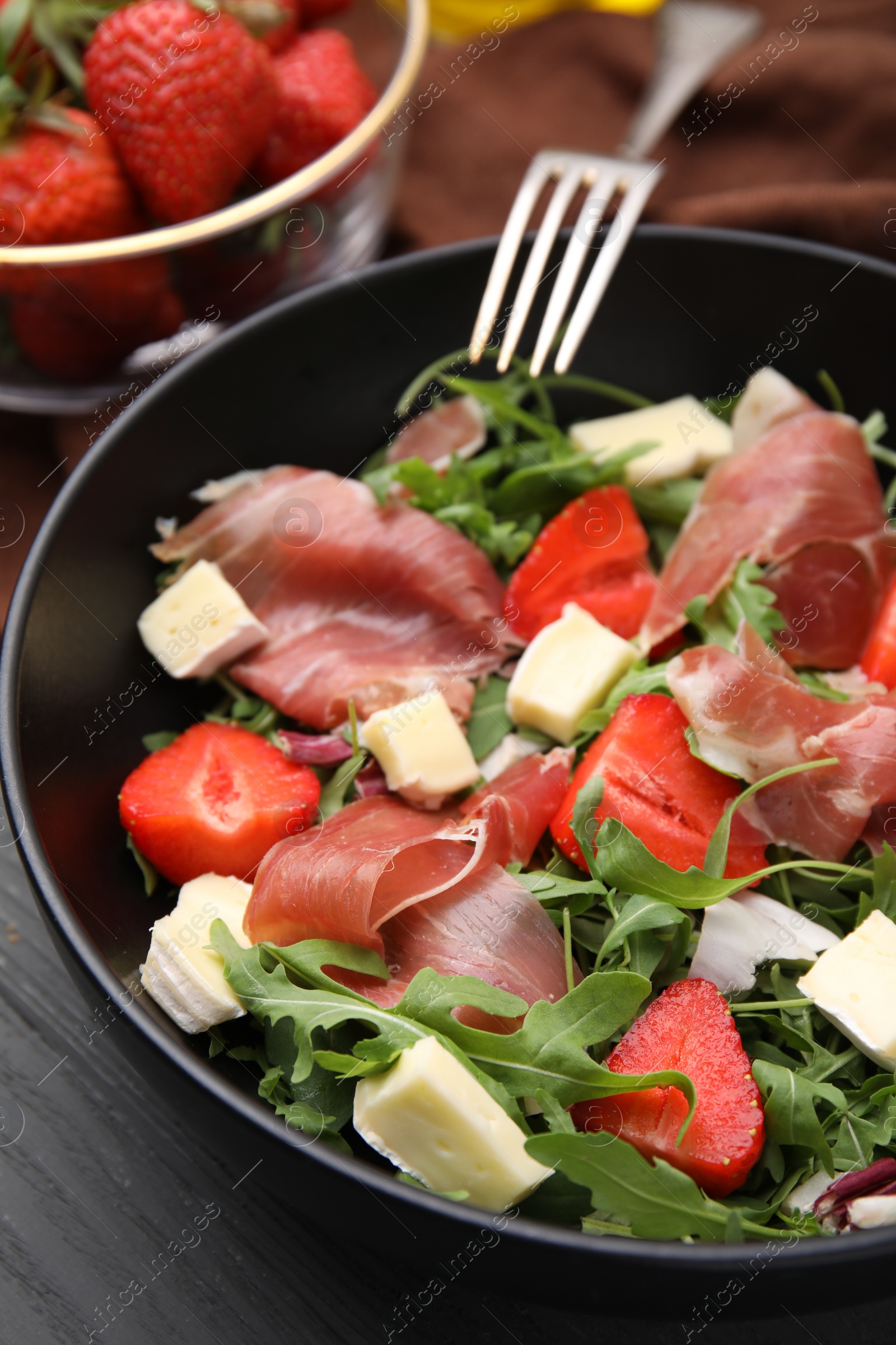 Photo of Tasty salad with brie cheese, prosciutto and strawberries on table, closeup