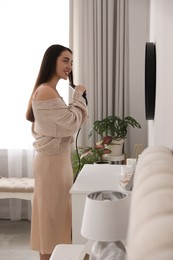 Photo of Young woman straightening hair near mirror at home. Morning routine