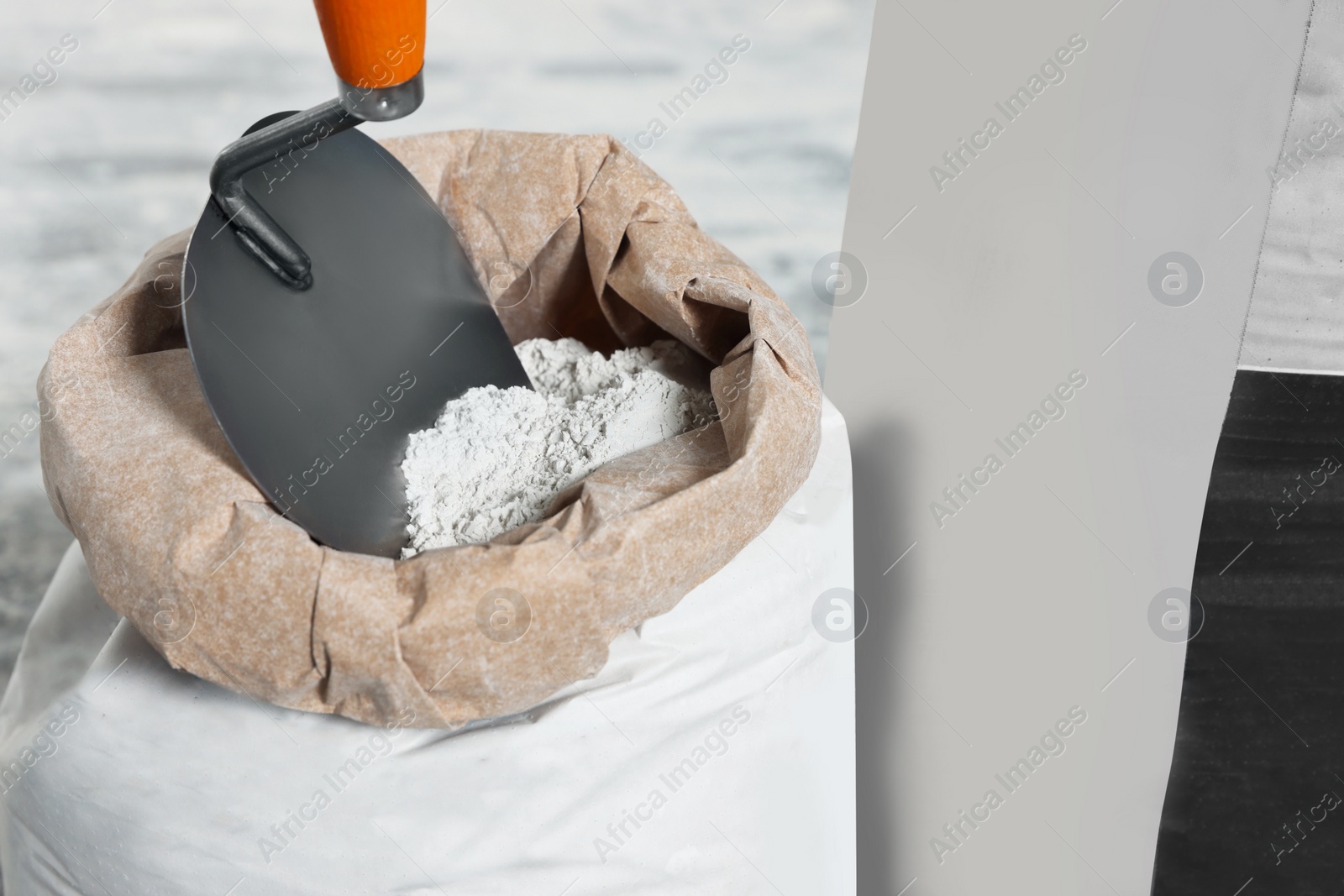 Photo of Cement powder and trowel in bag on blurred background, closeup