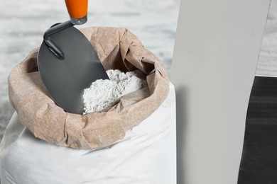 Cement powder and trowel in bag on blurred background, closeup
