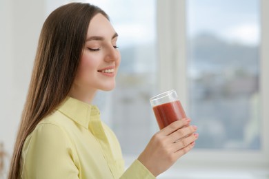 Photo of Beautiful young woman with delicious smoothie at home