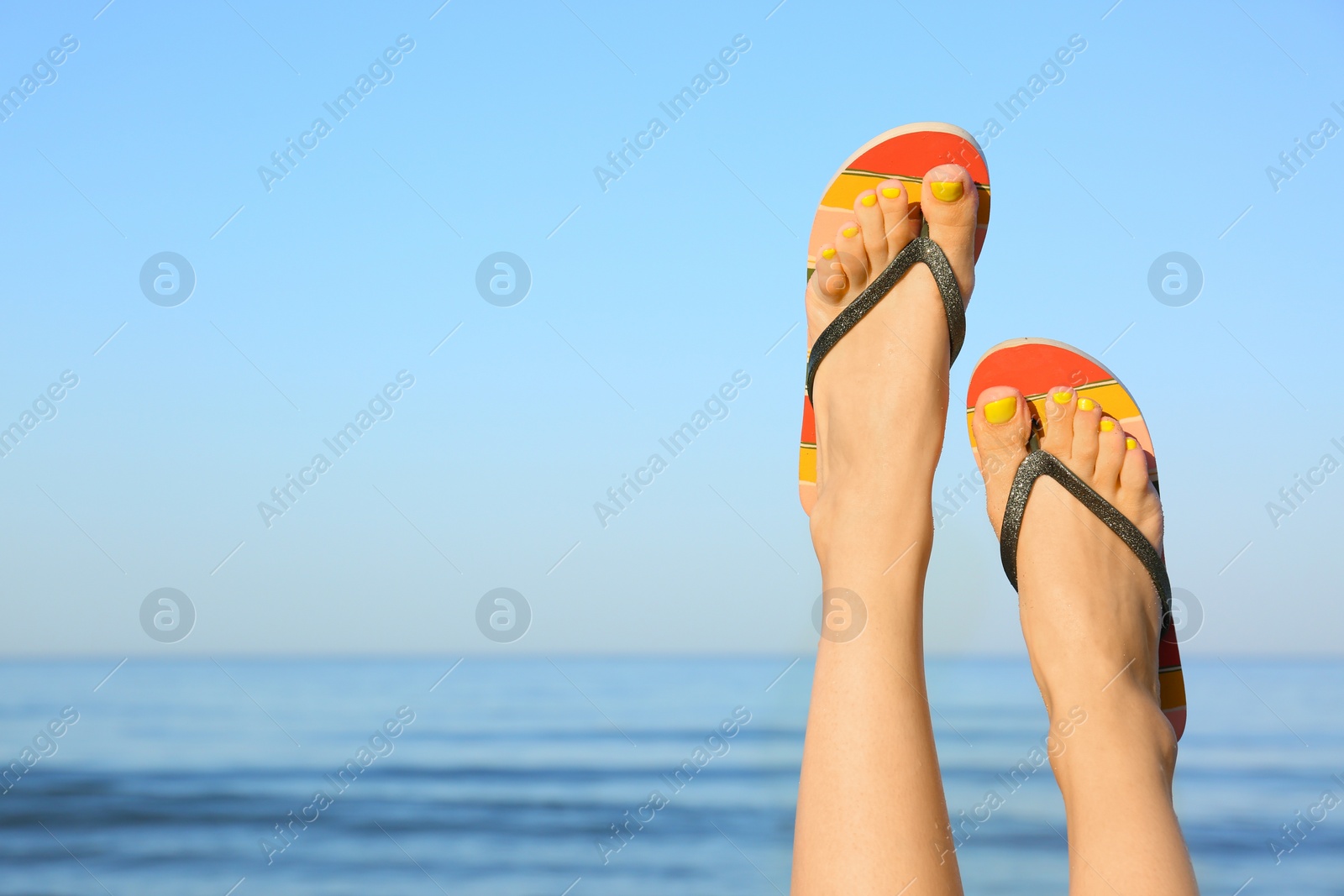 Photo of Closeup of woman wearing flip flops near sea, space for text. Beach accessories