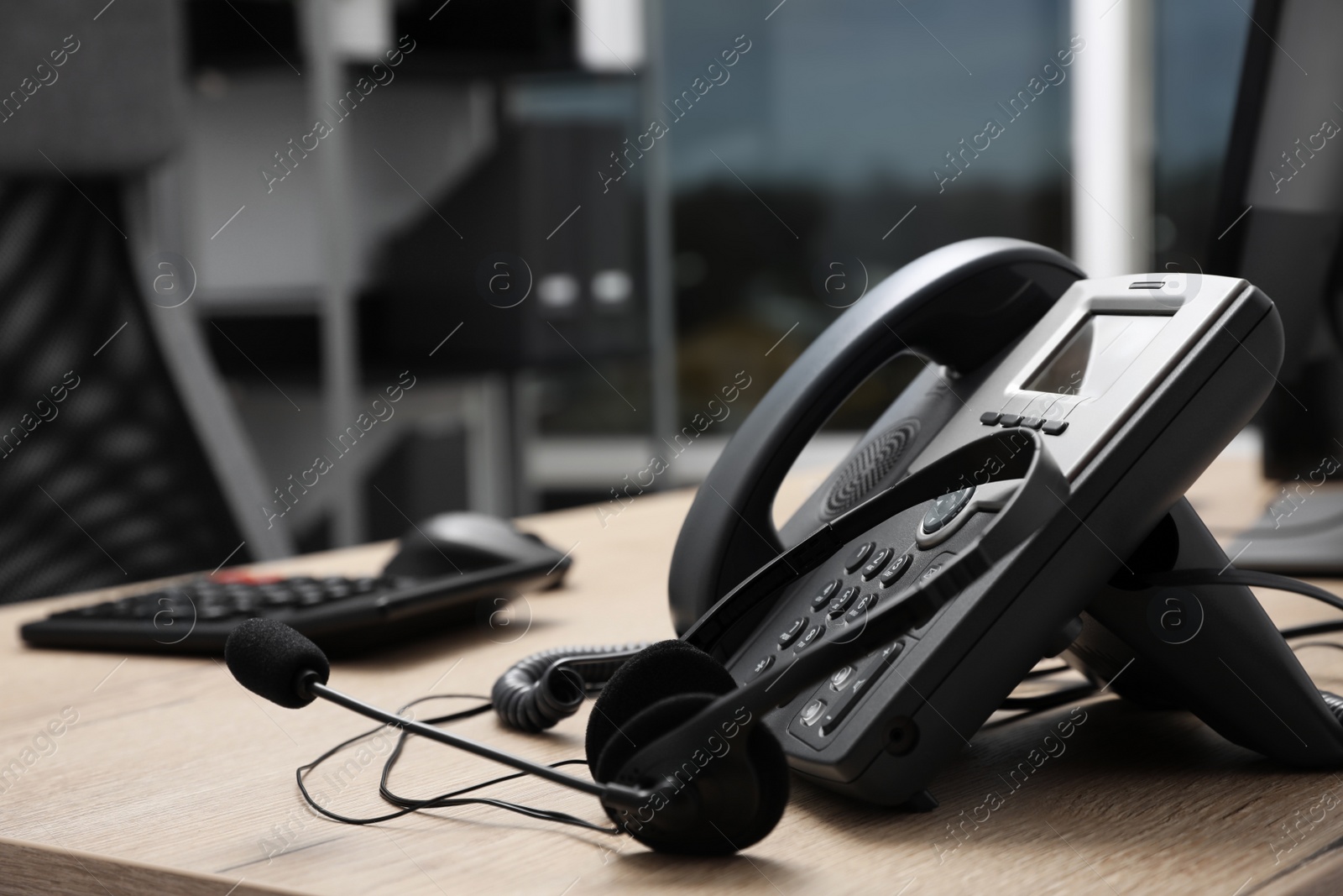 Photo of Stationary phone and headset on wooden desk indoors. Hotline service