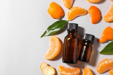 Aromatic tangerine essential oil in bottles, leaves and citrus fruit on grey table, flat lay. Space for text