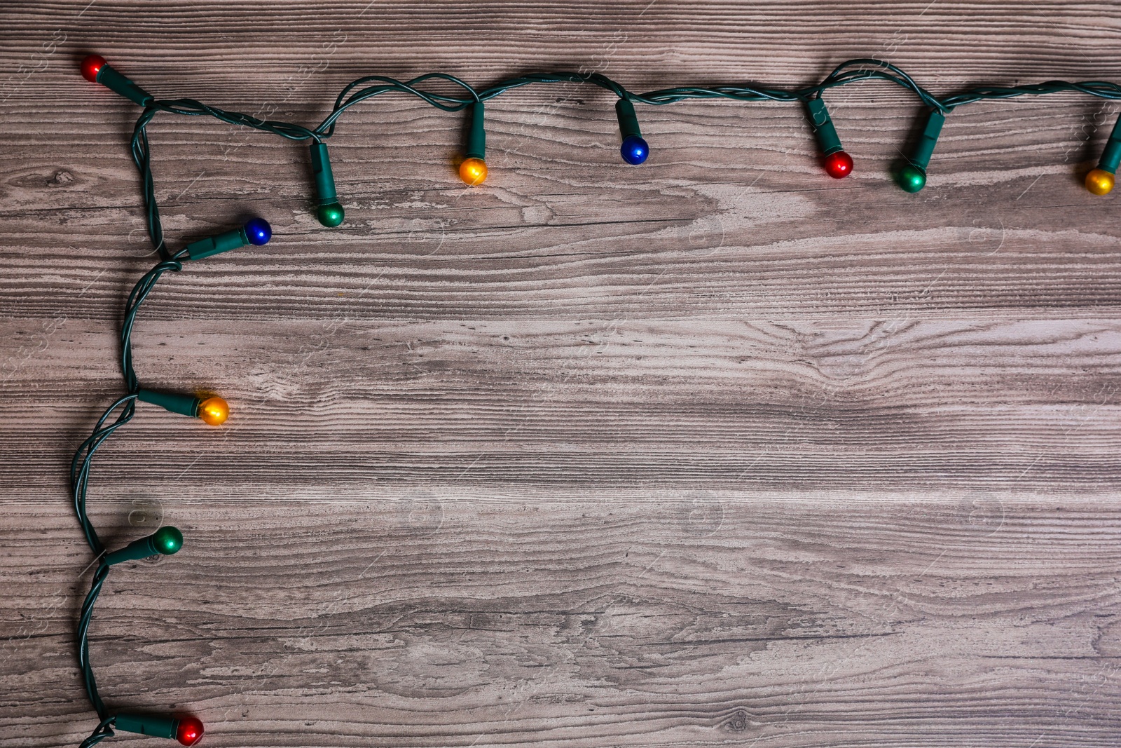 Photo of Christmas lights on wooden table, top view. Space for text