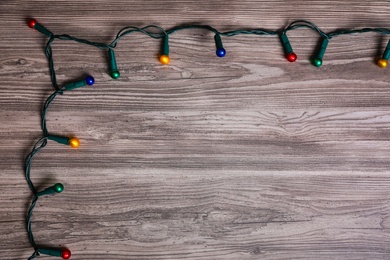 Photo of Christmas lights on wooden table, top view. Space for text