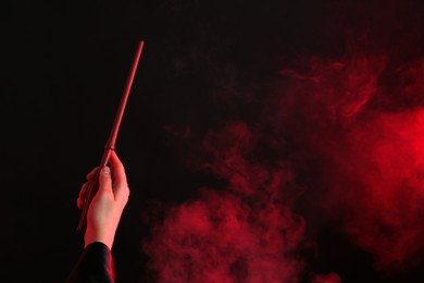 Photo of Magician holding wand in smoke on dark background, closeup. Space for text