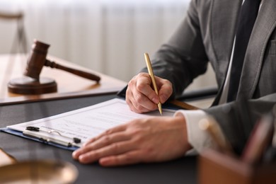 Photo of Notary writing notes at wooden table in office, closeup