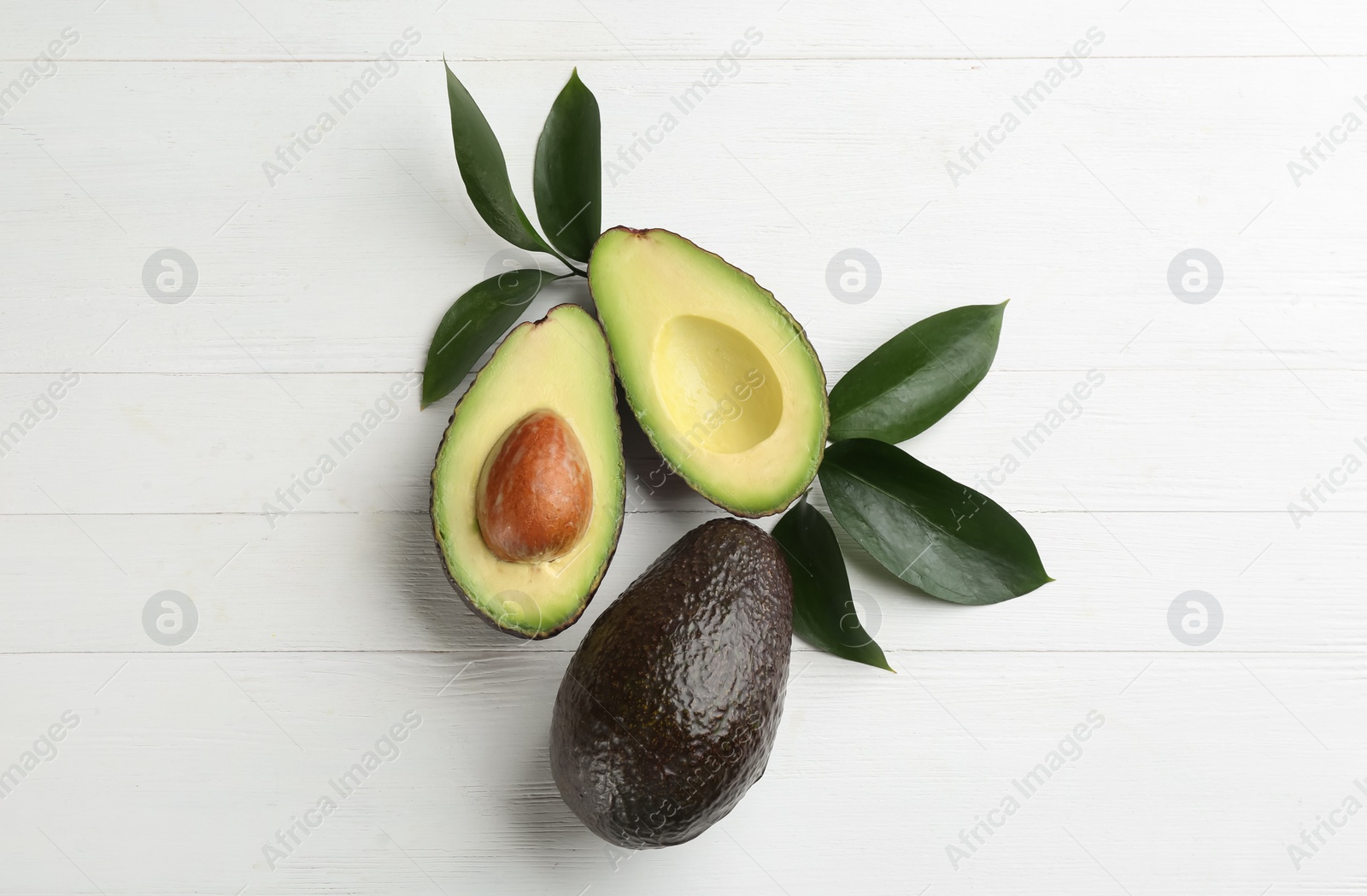 Photo of Whole and cut avocados with green leaves on white wooden table, flat lay
