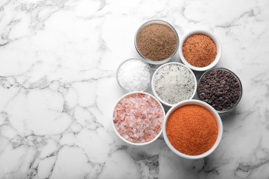 Different kinds of salt on white marble table, flat lay. Space for text