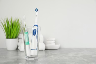 Electric toothbrushes in glass on light grey marble table, space for text. Dental care