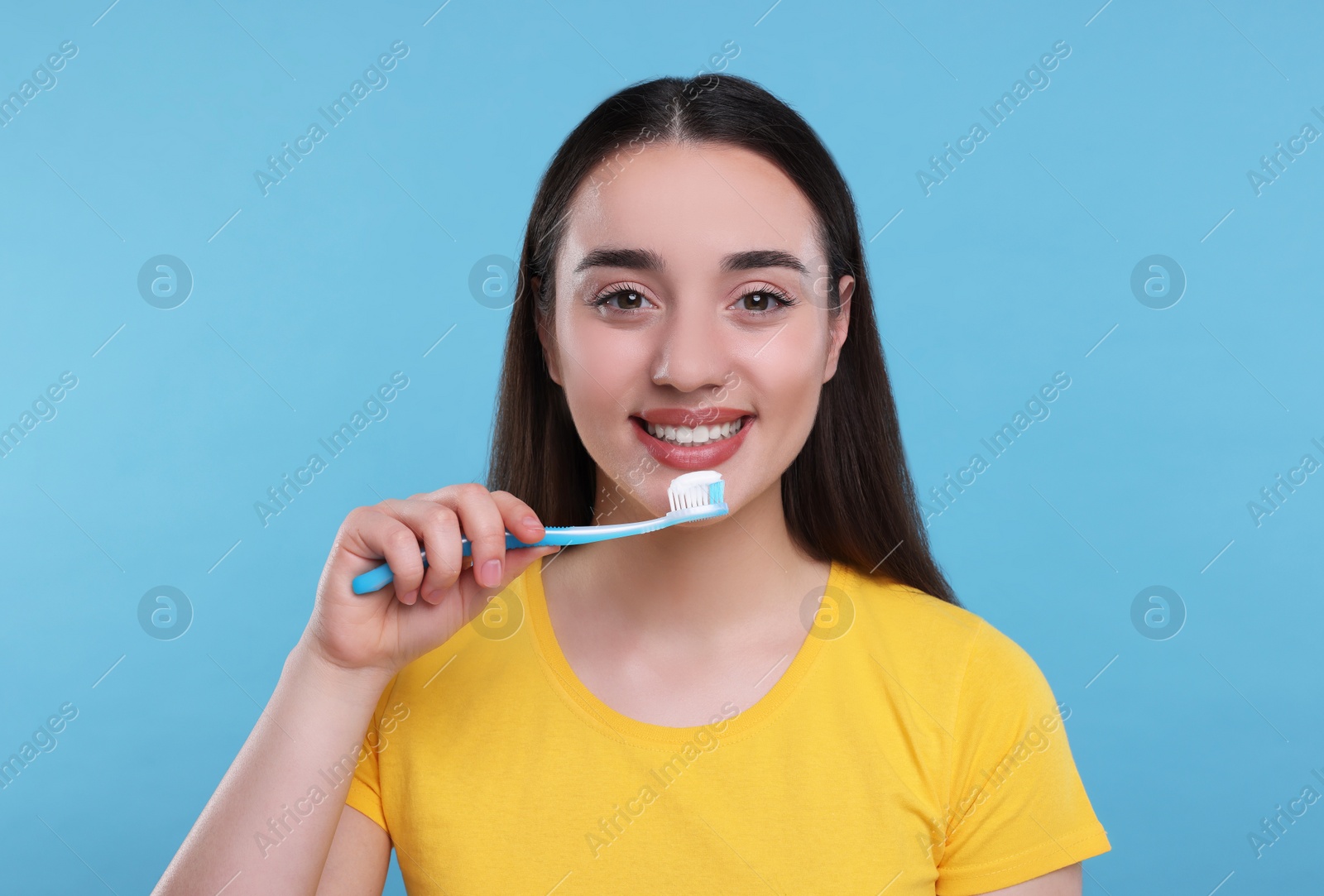 Photo of Happy young woman holding plastic toothbrush on light blue background