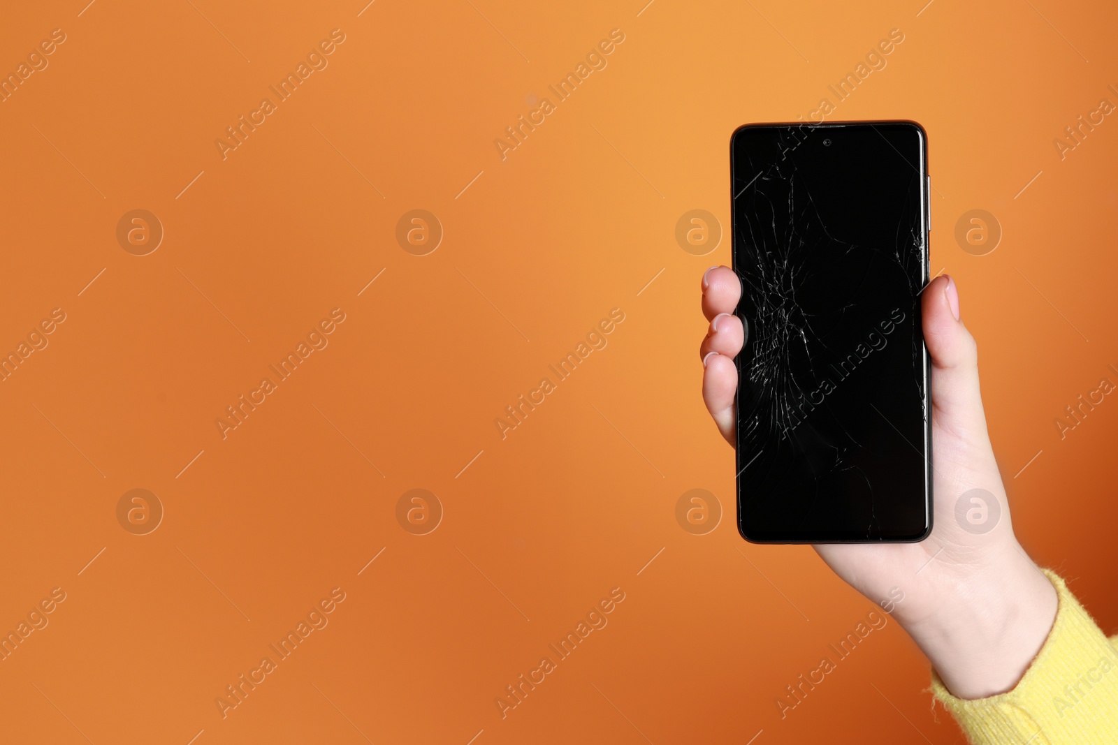 Photo of Woman holding damaged smartphone on orange background, closeup with space for text. Device repairing