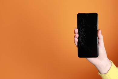 Woman holding damaged smartphone on orange background, closeup with space for text. Device repairing