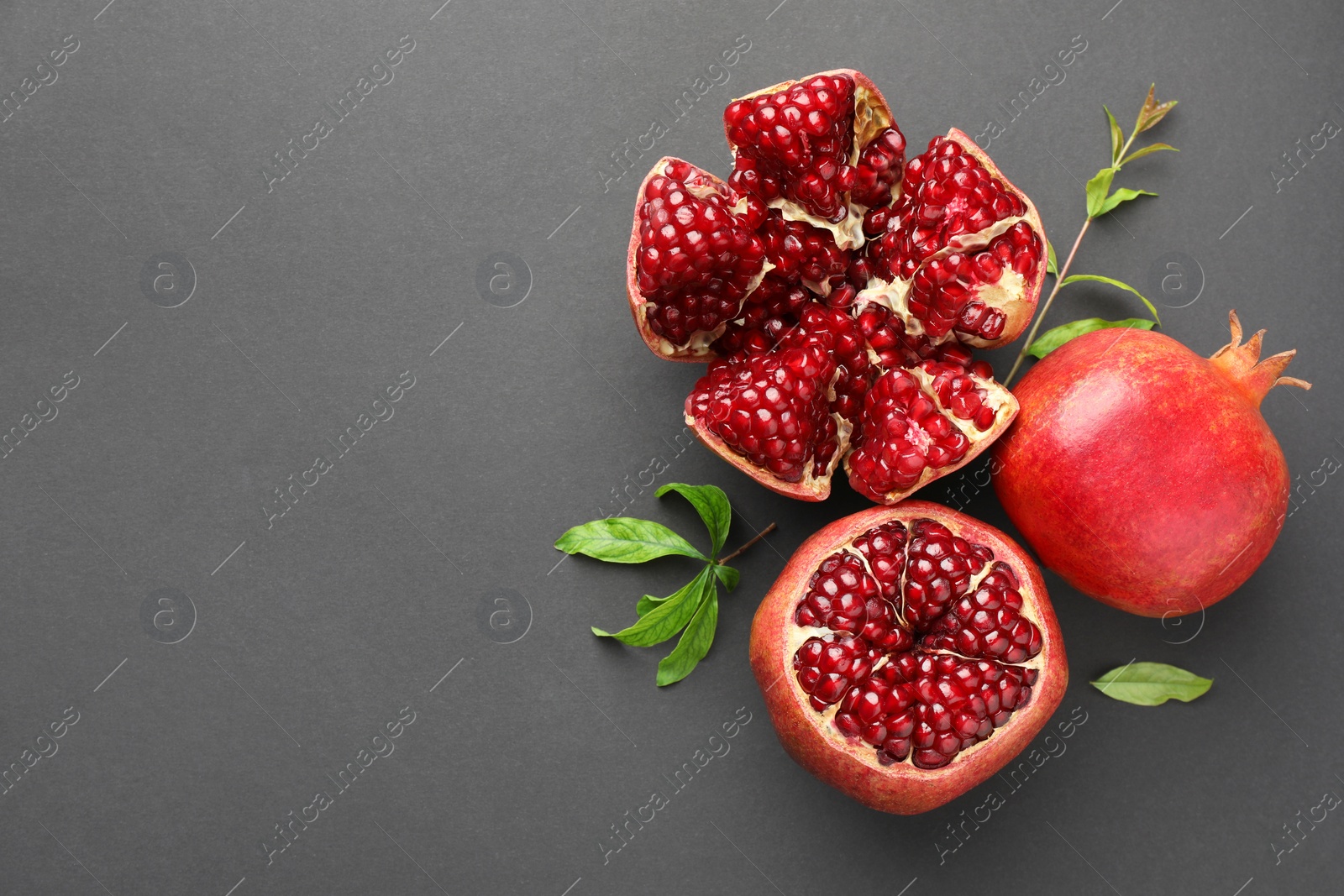 Photo of Fresh ripe pomegranates and leaves on grey background, top view. Space for text