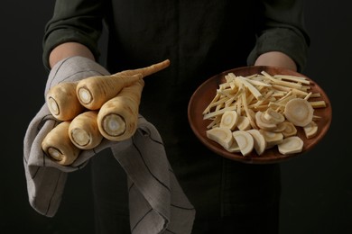 Photo of Woman holding whole and cut parsnips on black background, closeup