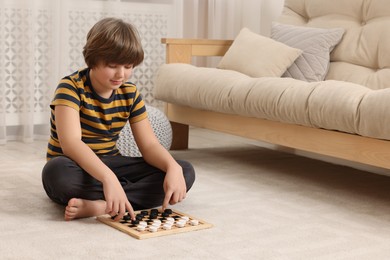 Photo of Playing checkers. Concentrated boy thinking about next move on floor in room