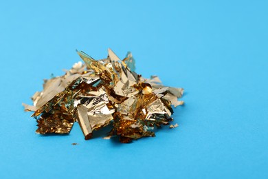 Photo of Pieces of edible gold leaf on light blue background, closeup. Space for text