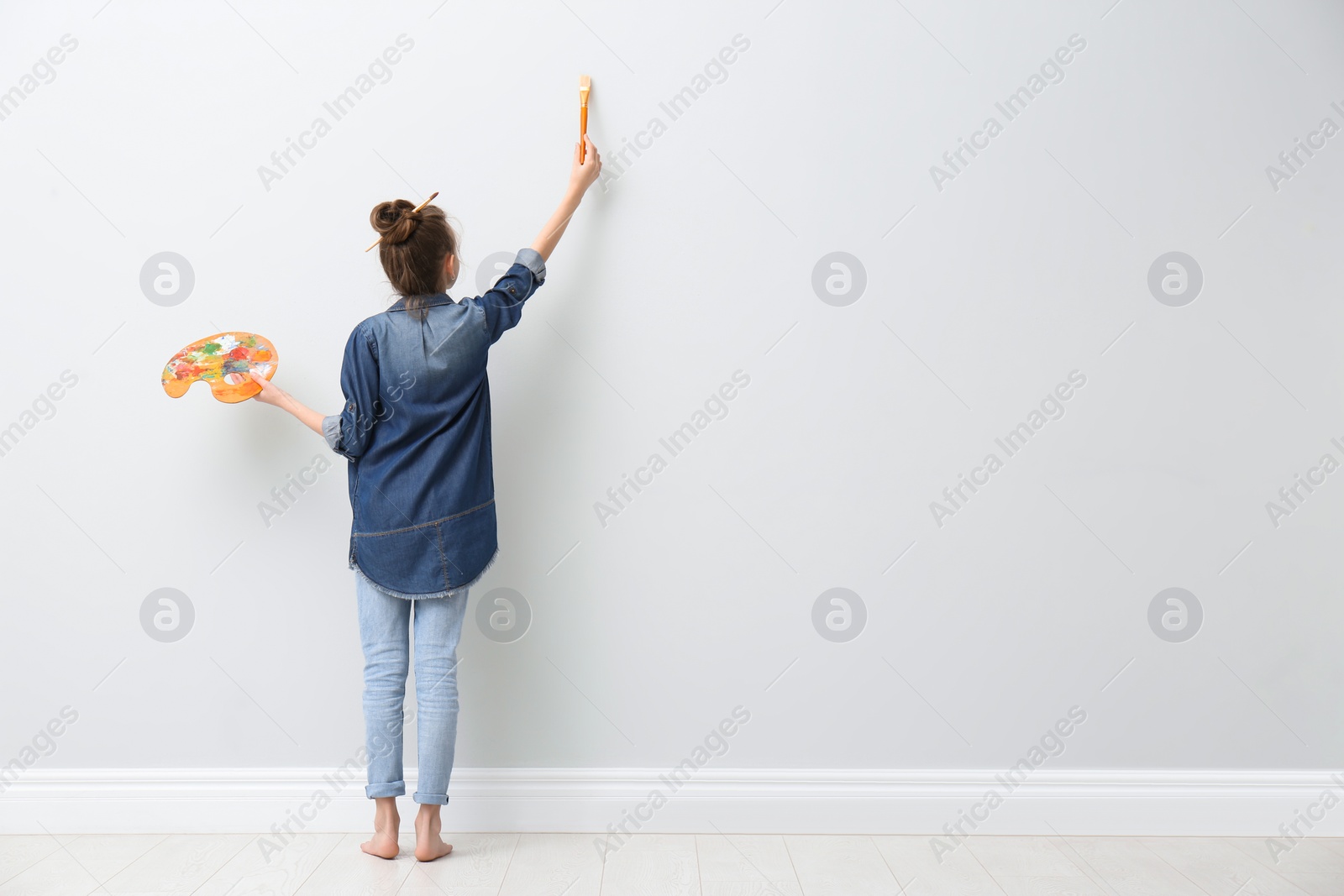 Photo of Little girl painting on light wall indoors, back view. Space for text