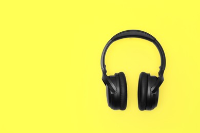 Modern wireless headphones on yellow background, space for text