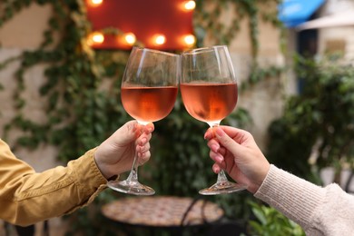 Photo of Women clinking glasses with rose wine outdoors, closeup