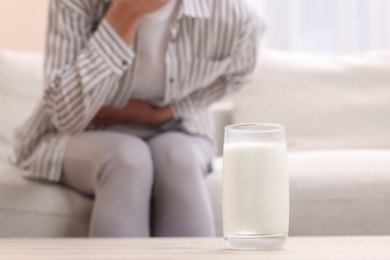 Woman suffering from lactose intolerance at home, focus on glass of milk. Space for text