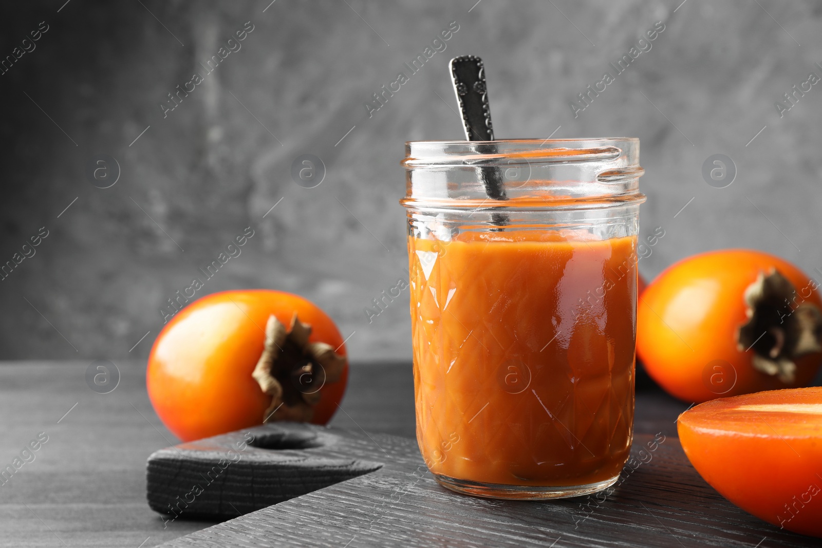 Photo of Delicious persimmon jam in glass jar served on dark gray wooden table, space for text