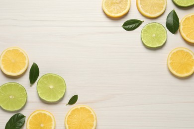 Fresh ripe lemons, limes and green leaves on white wooden background, flat lay. Space for text