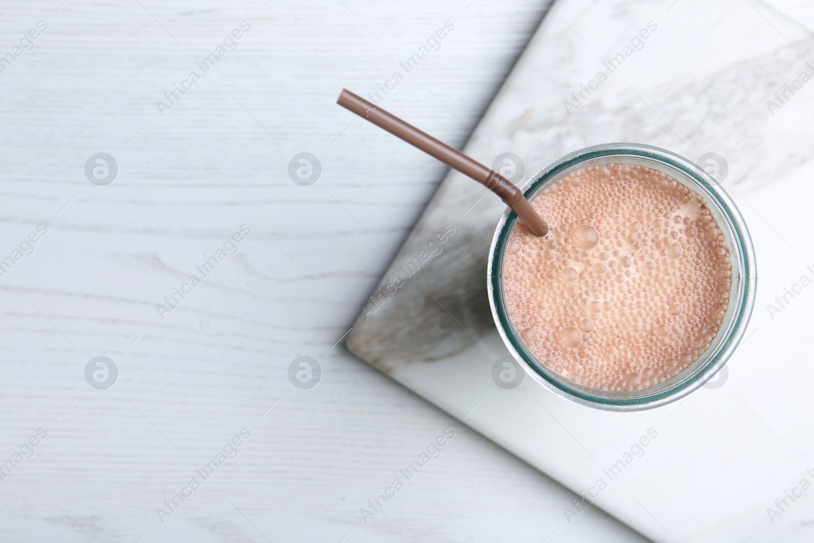 Photo of Glass with protein shake on white wooden table, top view. Space for text