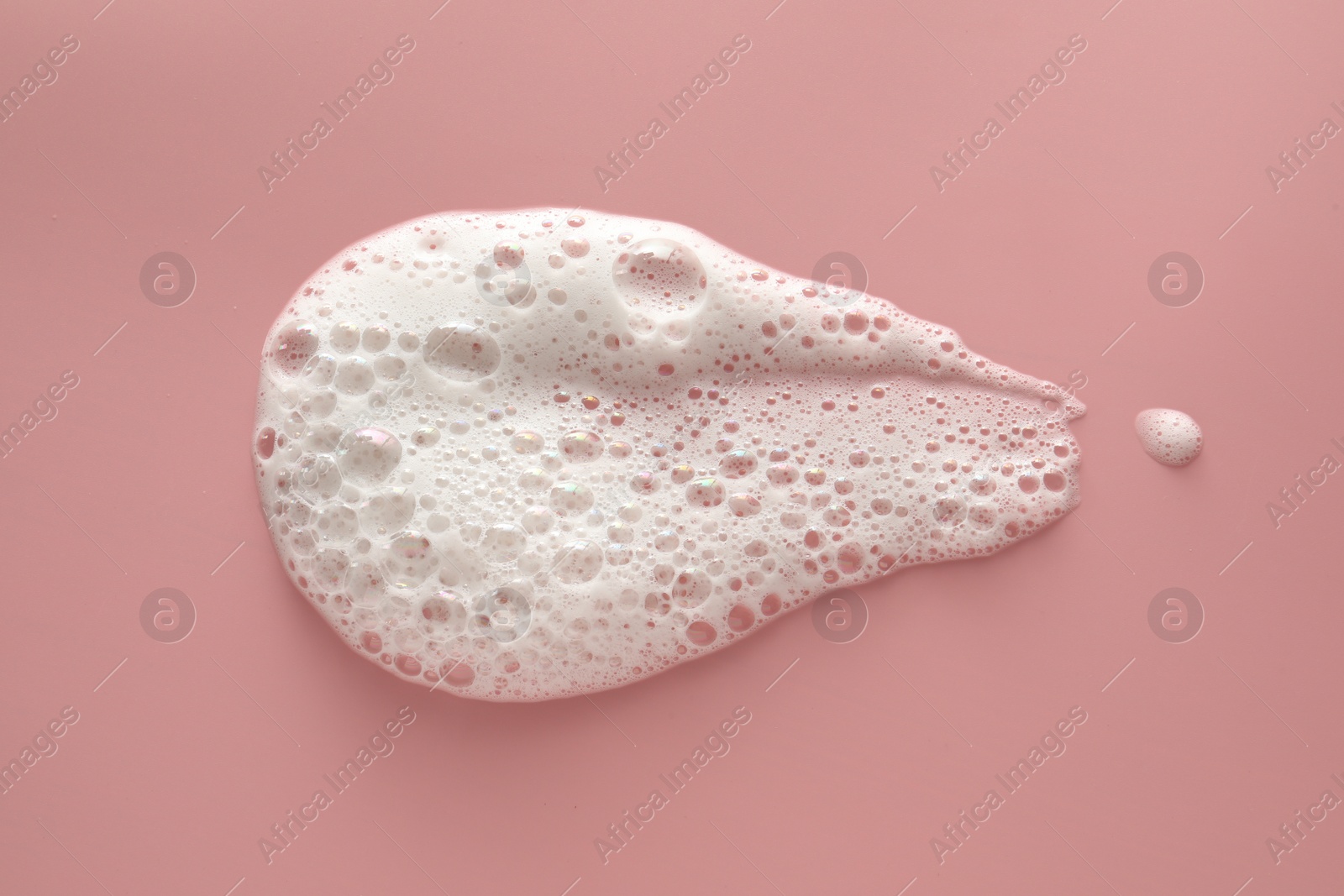 Photo of Spot of white washing foam on pale pink background, top view