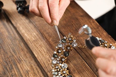 Photo of Male jeweler evaluating necklace at table in workshop, closeup. Space for text