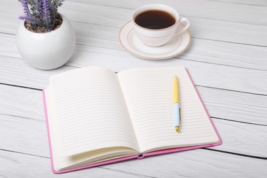 Photo of Open planner, pen, cup of coffee and lavender flowers on white wooden table