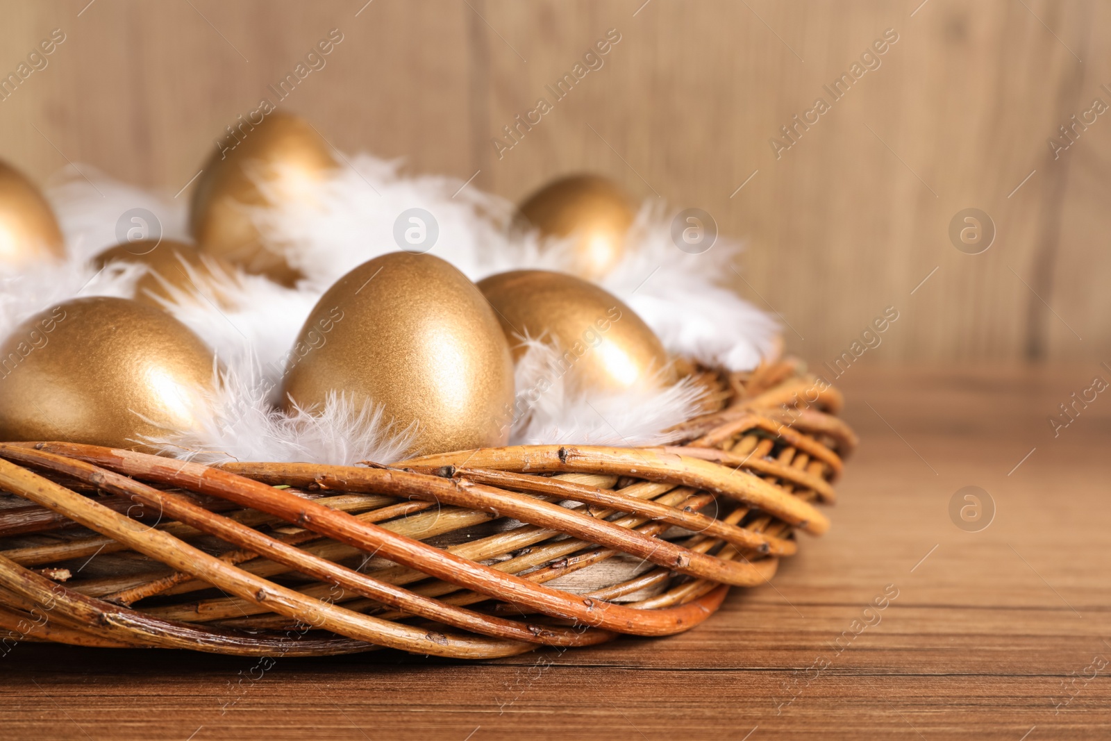 Photo of Golden eggs and feathers in nest on wooden table, closeup