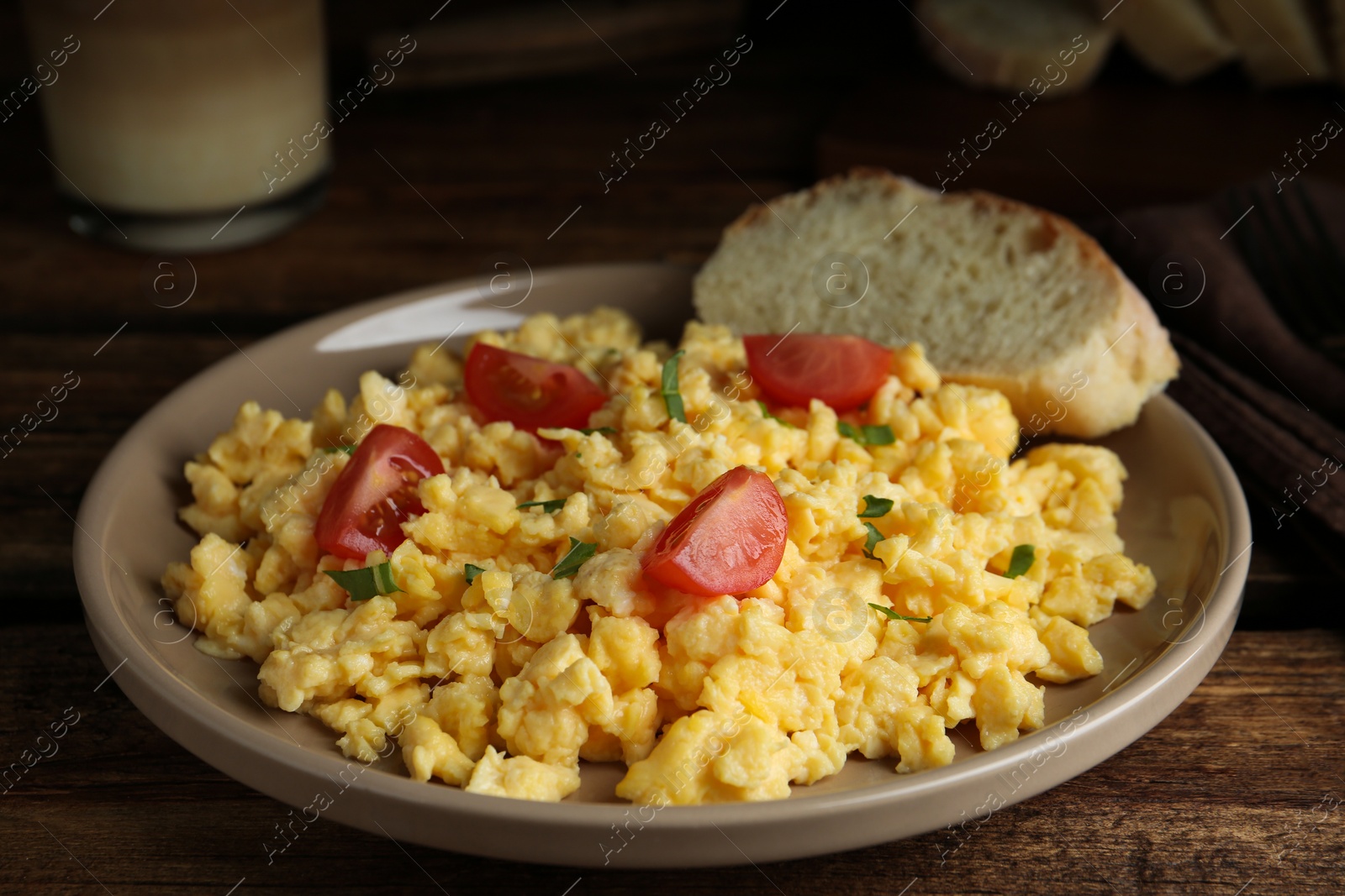 Photo of Tasty scrambled eggs with cherry tomato and bread on wooden table, closeup