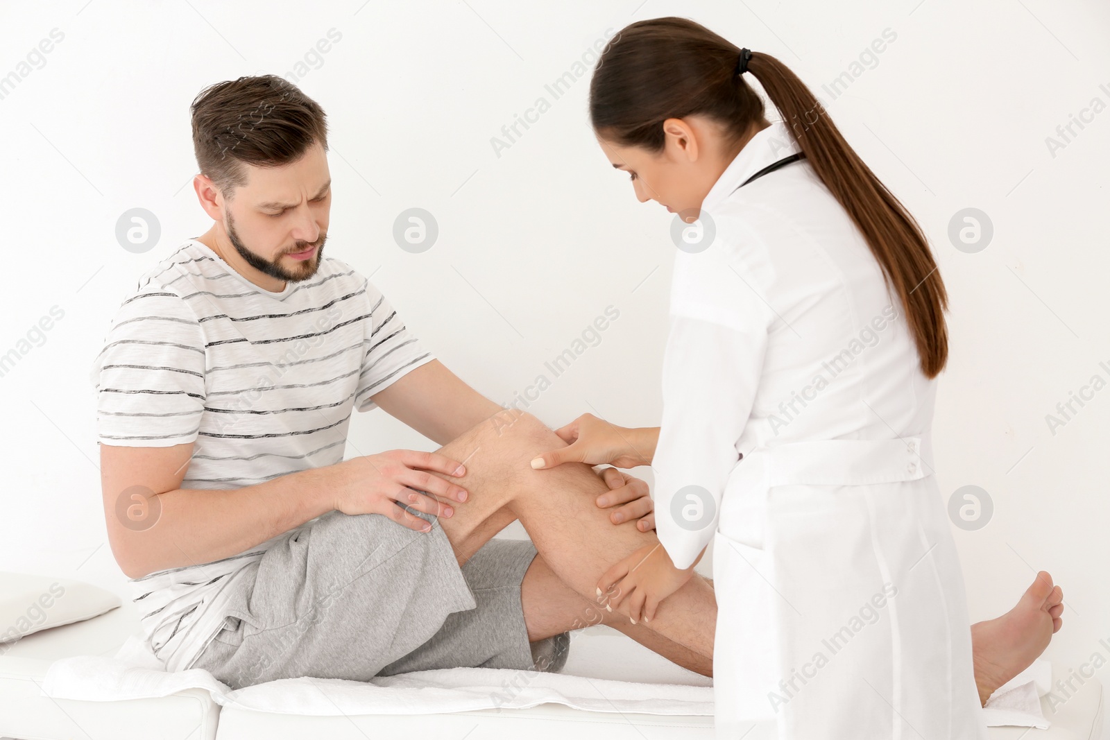 Photo of Doctor examining male patient with injured leg in clinic