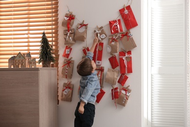 Photo of Cute little boy taking gift from Advent calendar at home. Christmas tradition