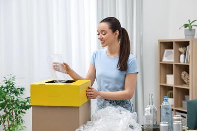 Garbage sorting. Smiling woman throwing plastic container into cardboard box in room
