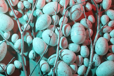 Photo of Many painted Easter eggs and tree twigs in blue neon light, flat lay